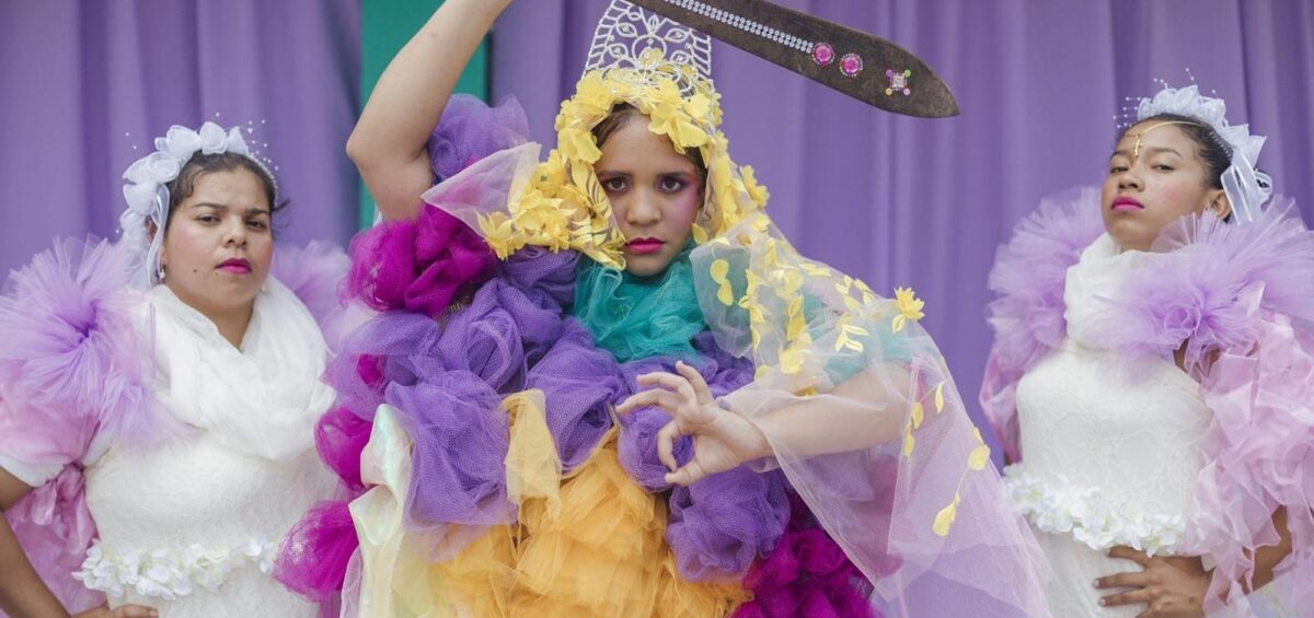 Lido Pimienta sosteniendo un machete, vestida de tul rosado, morado y naranja. Foto de Miss Colombia